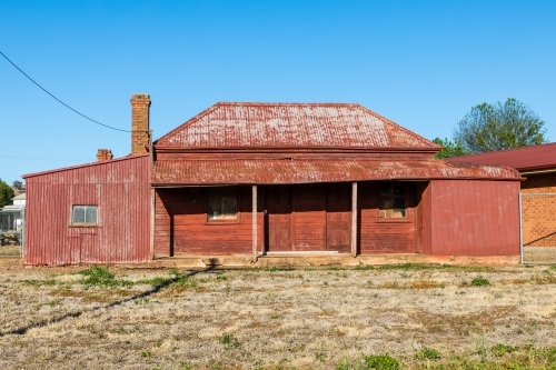 Red rusted, sun drenched, rundown, country house against a clear blue sky