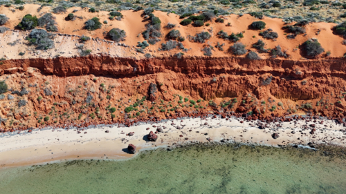 Red sandy cliff joining the ocean in remote area - Australian Stock Image