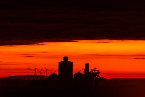 Red sky during dawn with the silhouettes of silos and wind turbines - Australian Stock Image