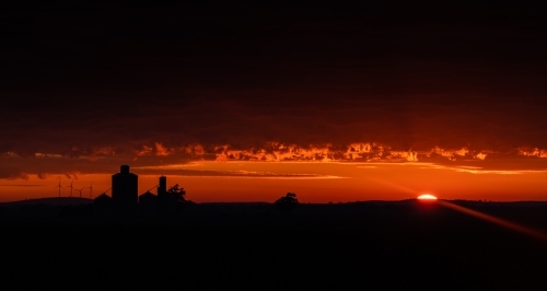 Red sky during sunrise with the silhouettes of silos and wind turbines - Australian Stock Image