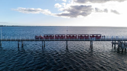 Red tourist train making its way along the pier - Australian Stock Image