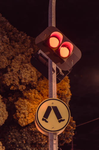 Red traffic light with pedestrian crossing sign at night - Australian Stock Image
