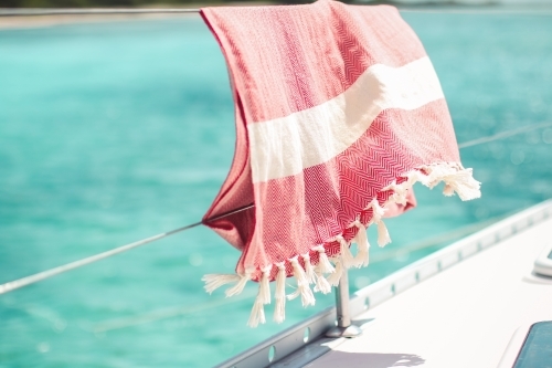 Red turkish towel hanging on wire railing of boat on the water - Australian Stock Image