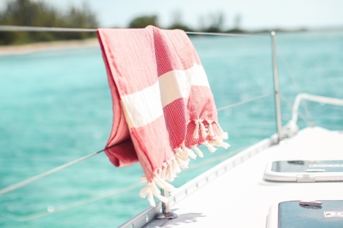 Red turkish towel hanging on wire railing of boat on the water - Australian Stock Image