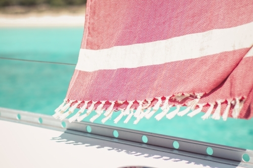 Red turkish towel hanging on wire railing of boat on the water - Australian Stock Image