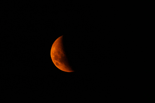 Reddish crescent moon in a dark sky - Australian Stock Image