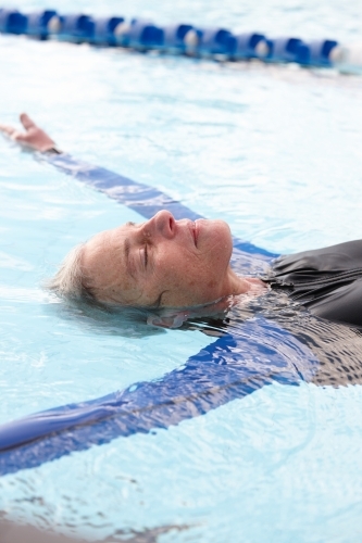 Relaxed active senior lady floating in swimming pool - Australian Stock Image