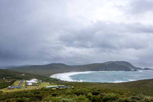 Remote coastal station overlooks windswept bay under heavy clouds and rugged hills - Australian Stock Image