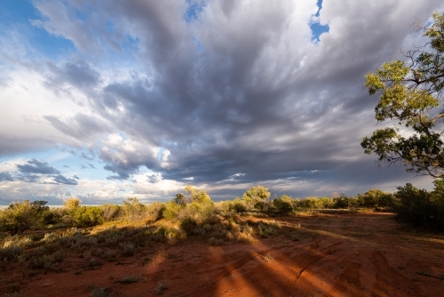Remote Desert landscape with stormy cloud patterns and long shadows in the red sand. - Australian Stock Image