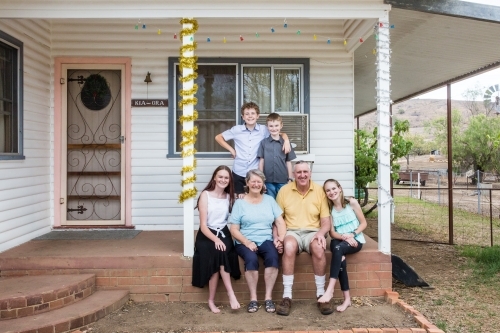 Retired grandparents sitting on front verandah of house with grandchildren happy - Australian Stock Image