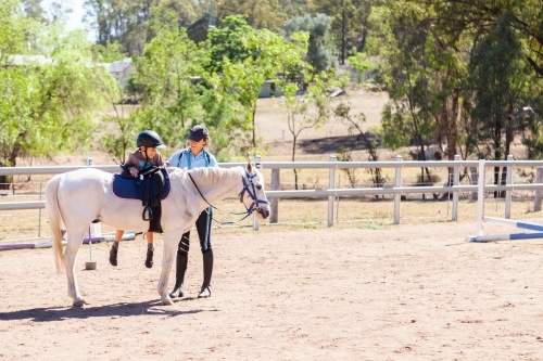 Riding instructor helping boy dismount pony - Australian Stock Image