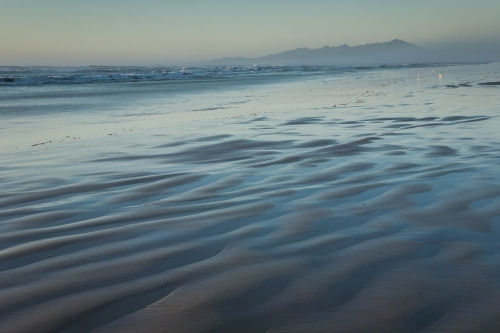 Ripples and blue water on beach with sea mist and distant mountains