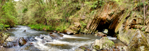 River flows through a tunnel in the rock surrounded by lush forest. - Australian Stock Image