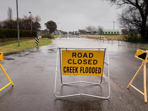 "ROAD CLOSED CREEK FLOODED" sign on underwater bitumen road - Australian Stock Image