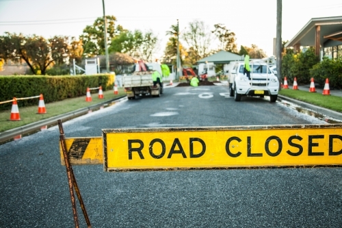 Road closed sign and water running over road from leaking water main - Australian Stock Image