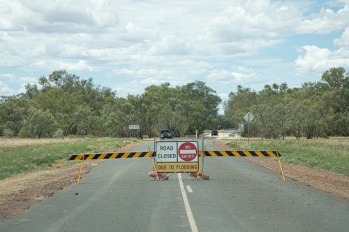 Road closed sign with vehicle driving through water behind - Australian Stock Image