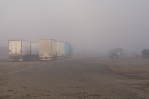 Road Trains parked at roadhouse shrouded in fog, Eyre Highway, South Australia - Australian Stock Image