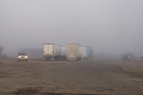 Road Trains parked at roadhouse shrouded in fog, Eyre Highway, South Australia - Australian Stock Image