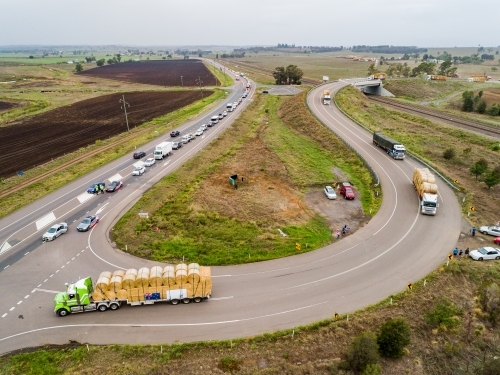 Road trains pulling out onto highway to continue journey delivering hay for drought relief - Australian Stock Image