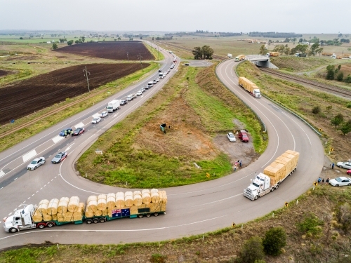 Road trains pulling out onto highway to continue journey delivering hay for drought relief