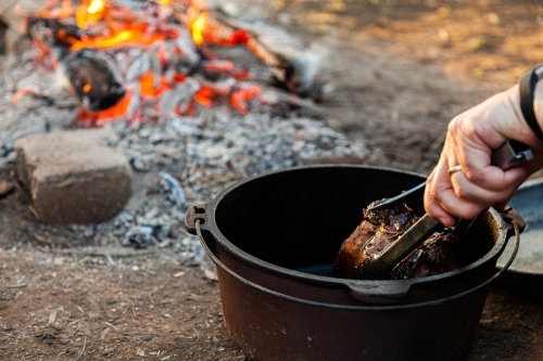Roast meat cooked in camp oven over fire - Australian Stock Image