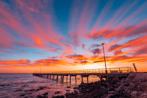Robe jetty with fishermen during sunrise while viewed from the shore. - Australian Stock Image