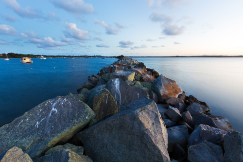 Rock breakwall symmetrically dividing calm boat harbour and the sea during tranquil sunset - Australian Stock Image