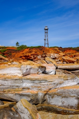 Rocky coastline with lighthouse tower against blue sky - Australian Stock Image