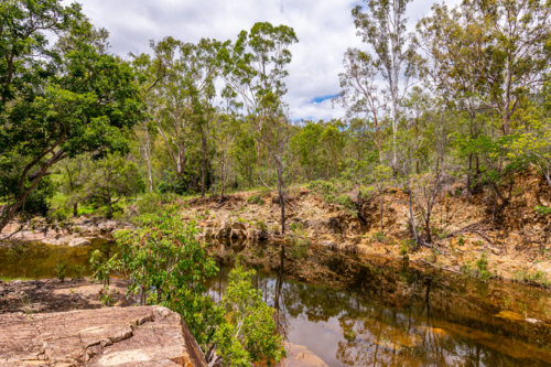 Rocky creek bed flowing through dense green bushland - Australian Stock Image