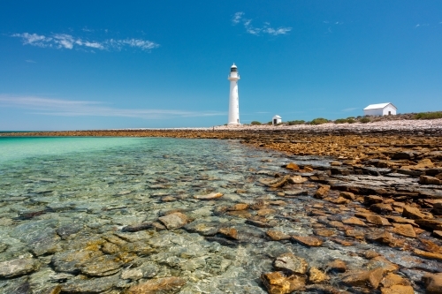 rocky shore with lighthouse and outbuildings under blue sky