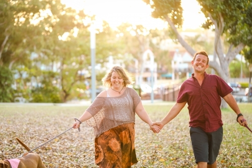 Romantic couple walking dogs in the park in golden afternoon light - Australian Stock Image