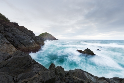 Rough ocean waves crashing against black rocks on an overcast day
