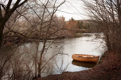 row boat docked on river side with ducks and trees in winter - Australian Stock Image