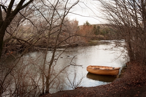 row boat docked on river side with ducks and trees in winter