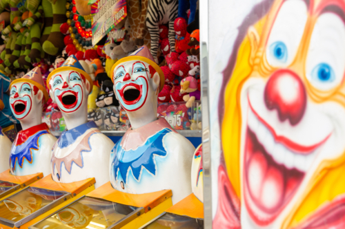 Row of brightly coloured clown heads at carnival sideshow alley - Australian Stock Image