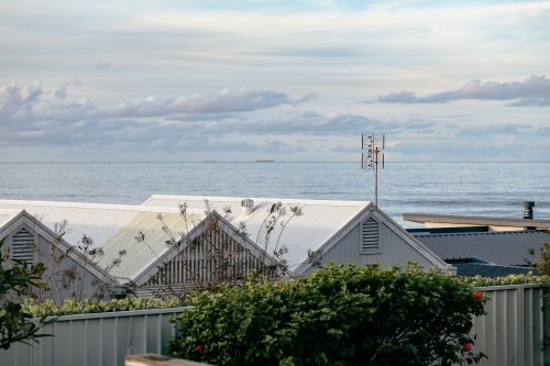 Row of pitched beach house roofs with sea in background in seaside town - Australian Stock Image