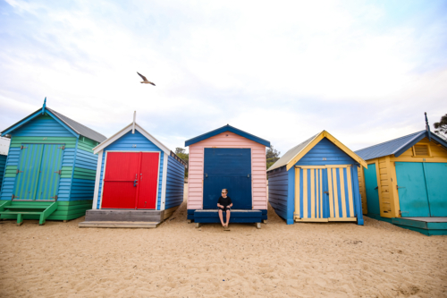 Row of vibrant beach huts with young boy sitting at centre - Australian Stock Image