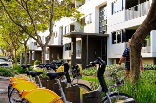 Row of yellow and orange push bikes lined up alongside the road in inner city living - Australian Stock Image