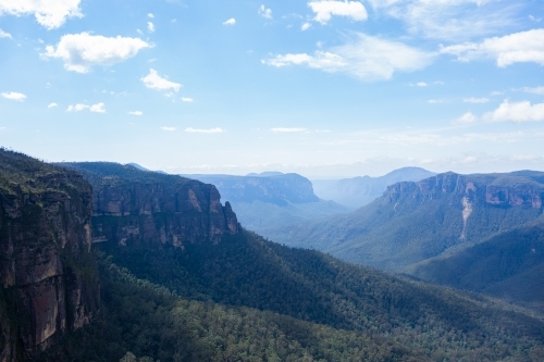 Rugged mountain ranges dip into tree filled valley seen from Govetts Leap - Australian Stock Image