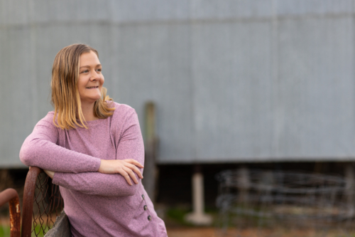 rural woman in her 30s resting her arm on a farm gate near a shed - Australian Stock Image