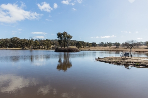 Rustic seat overlooking river water with trees on farm - Australian Stock Image
