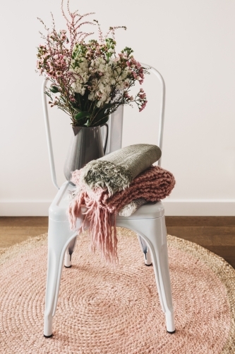 Rustic styled vase of flowers with wool scarves on a white chair - Australian Stock Image