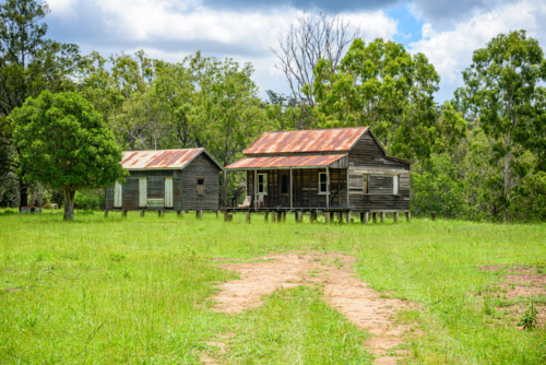 Rustic timber homesteads on wooden stumps with rusty corrugated iron roofs in rural landscape - Australian Stock Image