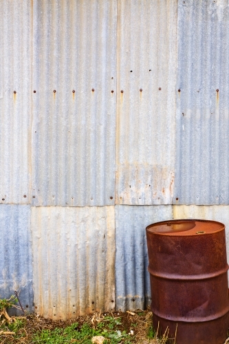Rusty drum in front of corrugated iron wall - vertical - Australian Stock Image