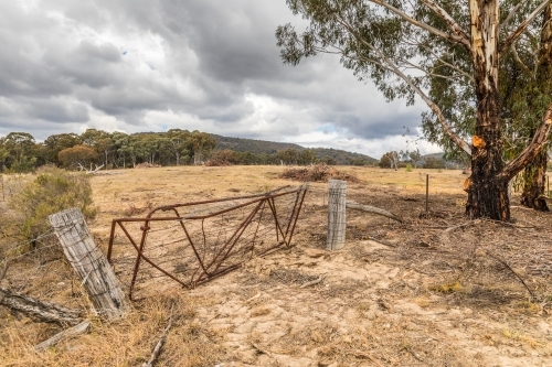 Rusty old gate and wire fence with old wooden posts along a dry property - Australian Stock Image