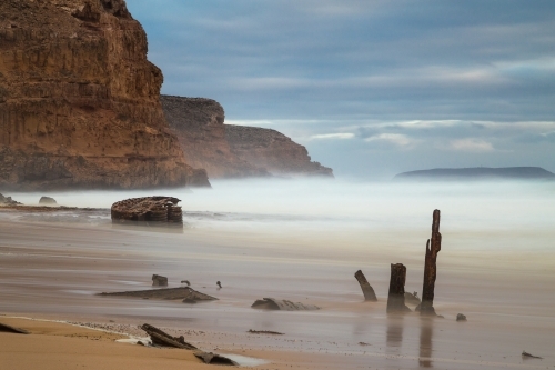Rusty pieces of a shipwreck sticking out of the sand on an isolated beach - Australian Stock Image