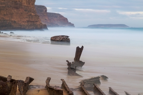 Rusty pieces of a shipwreck sticking out of the sand on an isolated beach - Australian Stock Image