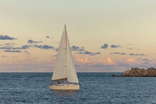 Sail boat entering the Hunter River past the Nobby's Beach breakwall at Newcastle, NSW - Australian Stock Image