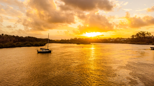 sailing boat at vibrant sunset reflections on wide river estuary - Australian Stock Image