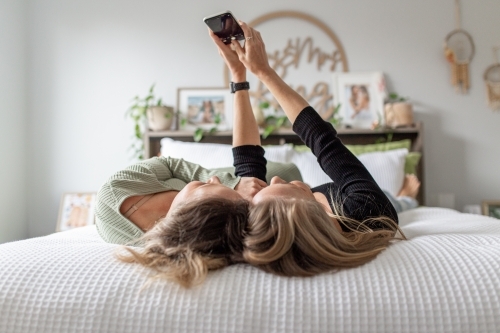 Same sex female couple lying on a bed taking a selfie - Australian Stock Image